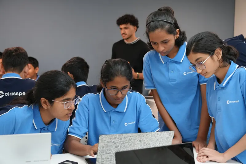 Four students gather around a laptop during a group workshop activity.