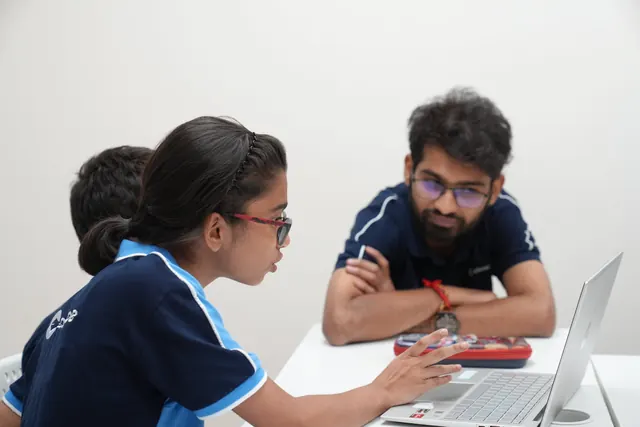 A student discusses her laptop work with a mentor across the table.