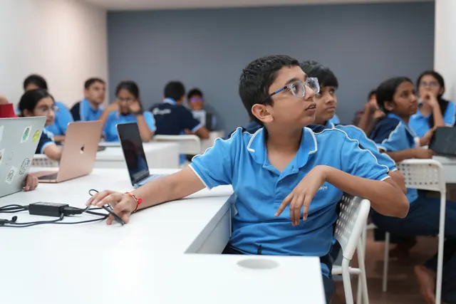 A student listens during the workshop, with classmates and laptops nearby.